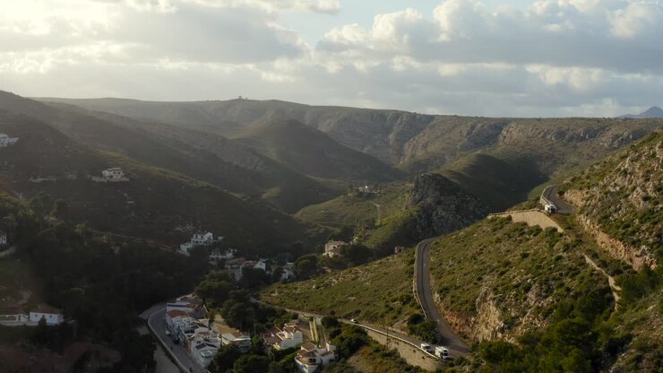 Lunga ripresa aerea che si allontana da strade collinari tortuose e case verso una splendida baia mediterranea azzurra e appartata in Spagna, verso il tramonto