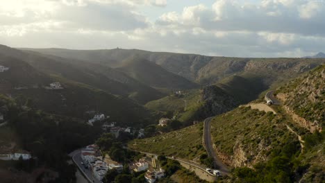 toma aérea larga volando hacia atrás desde las sinuosas carreteras y casas de las laderas hasta una hermosa bahía mediterránea azul aislada en españa alrededor de la puesta del sol