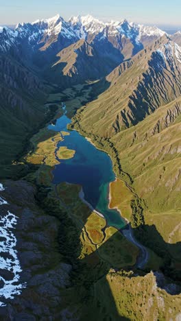 Aerial view of a winding river through a lush valley with snow-capped mountains