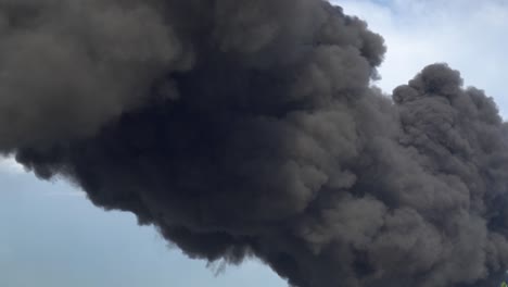 black smoke rises above the buildings. a big chemical fire at a factory building. thick black smoke covers the sky.