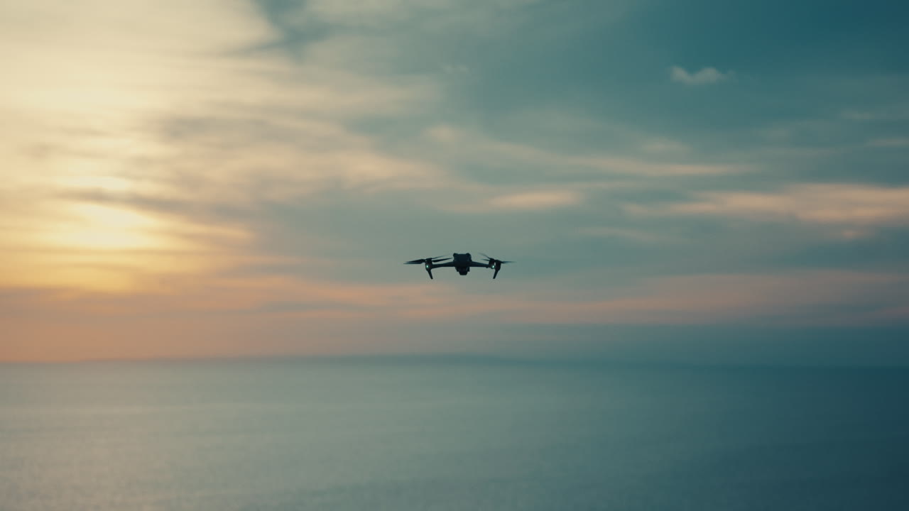 En professionel drone flyver over det rolige hav under en levende solnedgang og fanger essensen af luftteknologi og moderne udforskning.