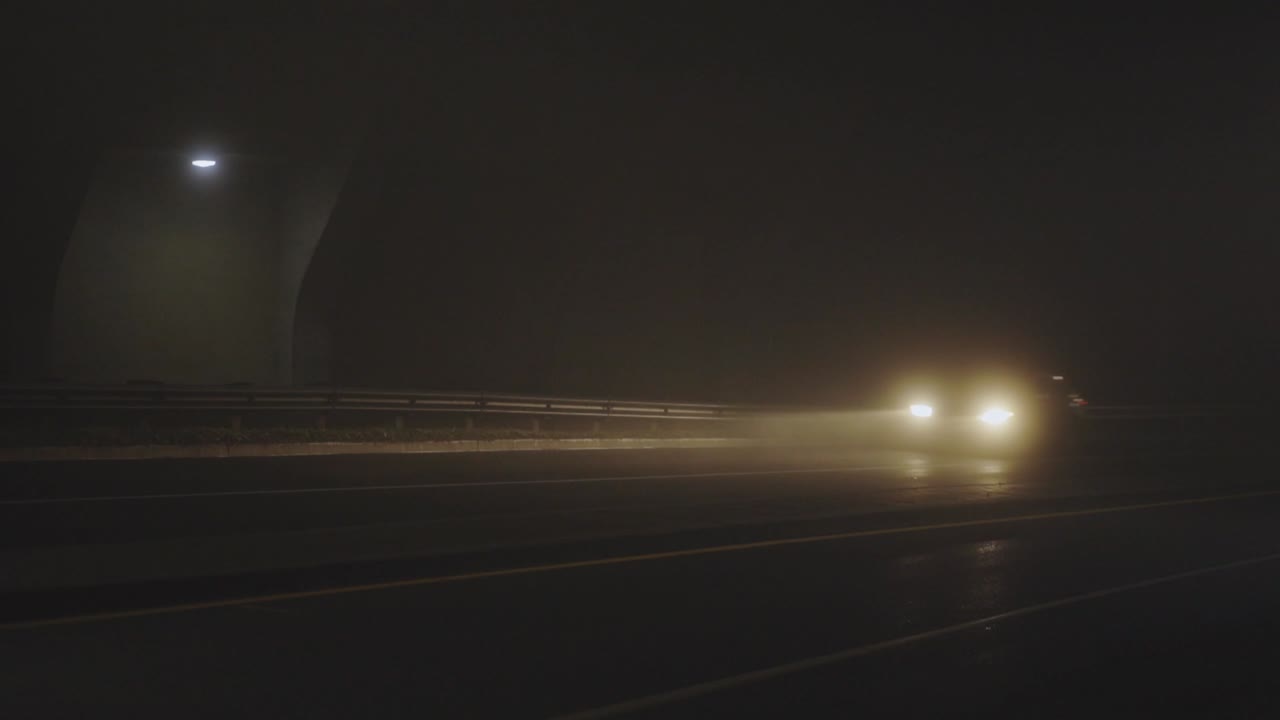안개가 자욱한 저녁에 어두운 다리 아래에서 자동차가 속도를 냅니다.