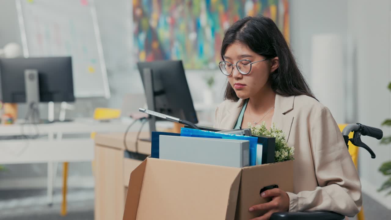 Sad disillusioned disappointed young woman with glasses with sorrow leaves her job in the company, she was fired by disability, illness, wheelchair, injustice of employer, boss, unemployment