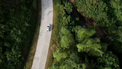 Vista-Aérea-Siguiendo-Un-Coche-Blanco-En-Una-Carretera-Pavimentada-Conduciendo-A-Través-Del-Bosque-Tropical