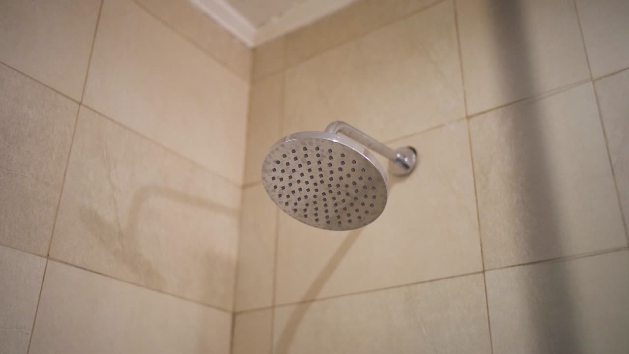 Slow moving camera shot of aluminum shower interior at hotel. Light beige color tiles in wall background.