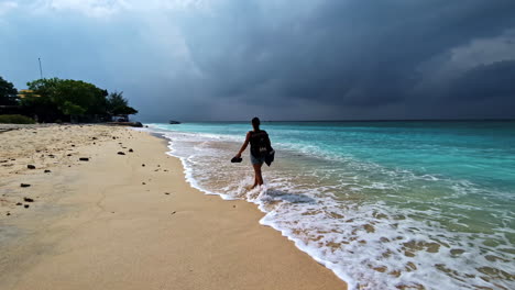woman with backpack and barefoot walking along sandy beach on a cloudy day in indonesia