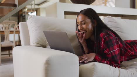 Mixed-race-woman-on-couch-at-home-using-laptop-having-video-chat