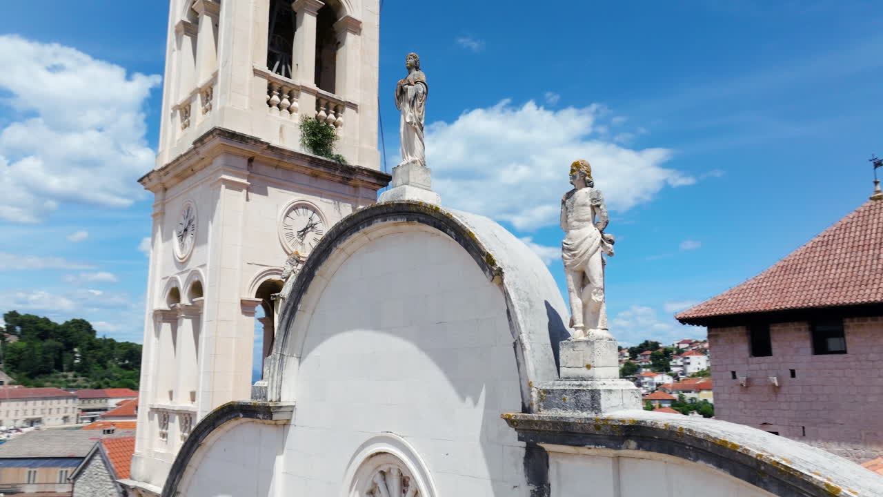 Saint John’s Church In Seaside Town Of Jelsa, Hvar Island, Croatia. Statues Atop Historic Facade With Clock Tower. orbiting drone shot