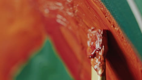 close-up of brush coated in orange paint creating textured strokes on canvas