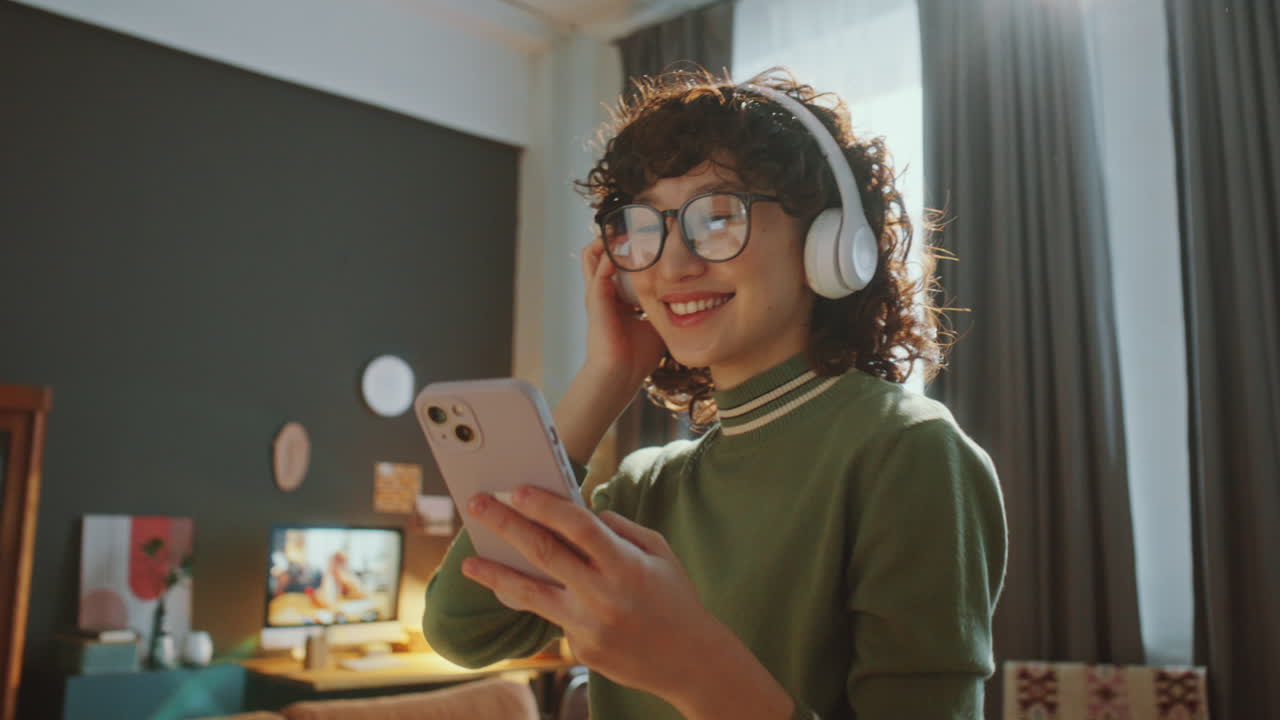 Joyful Asian Girl in Headphones Dancing with Phone at Home