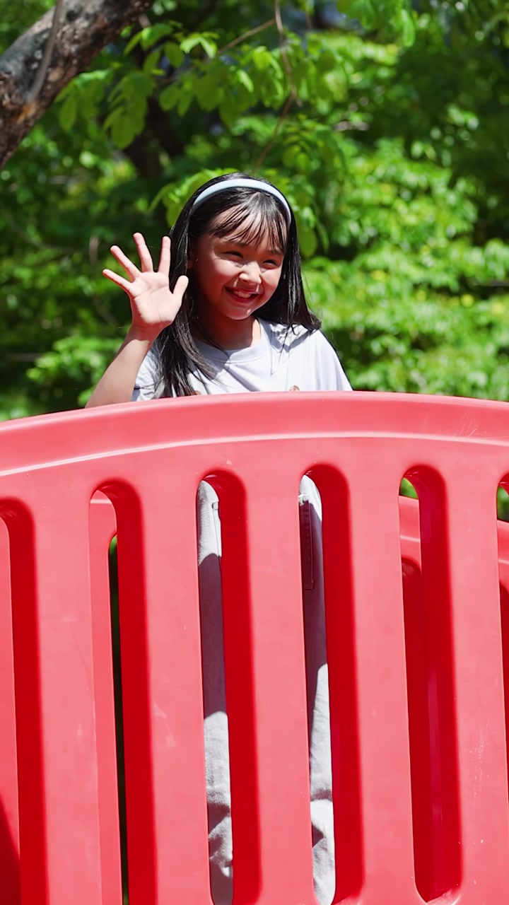 Happy Asian child waves from a red bridge at Lumpini Park under bright natural sunlight