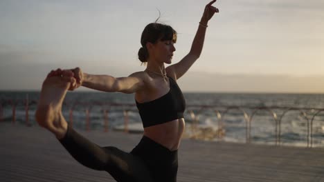 mujer practicando yoga junto al océano al atardecer