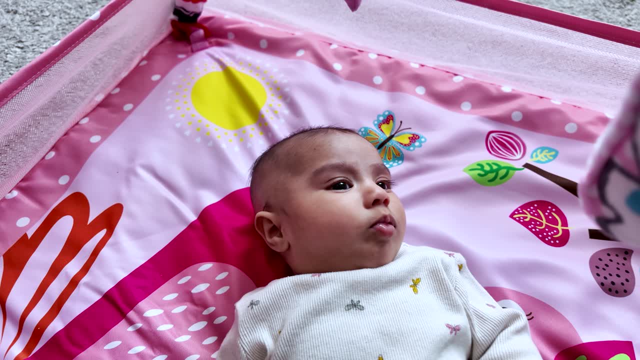 Three month old baby girl lies on a pink play mat, enjoying her playtime. slow motion