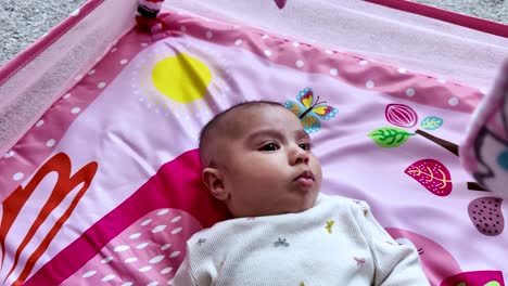 three month old baby girl lies on a pink play mat, enjoying her playtime. slow motion