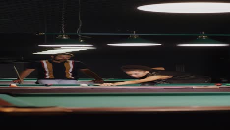 couple playing billiards in a dark bar