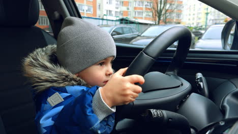 happy energetic toddler boy jumps up sitting on the driver's seat. lovely kid holding the steering wheel. close up.