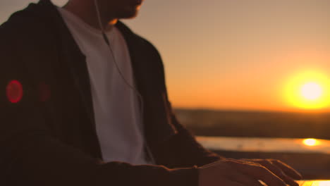 vault plan of a hand typing on a laptop keyboard at sunset with a view of the city from a height. programmer working on the roof of a building.