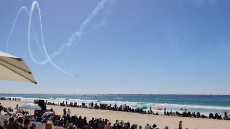 planes perform stunts above a busy beach scene