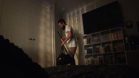 a man enters his room, lit by the golden rays of the setting sun filtering through blinds. he sets his cricket bag and bat down, then jumps onto the bed, reflecting a moment of exhaustion and peace.