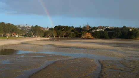 drone flying forward on a beach through rain towards a rainbow at the end of the beach