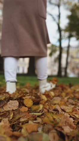 woman walking through autumn leaves in city park