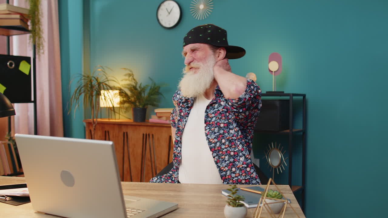 노인이 노트북 화면을 보고 집에서 목과 허리 통증으로 고통받는 동안 춤을 추고 있습니다.