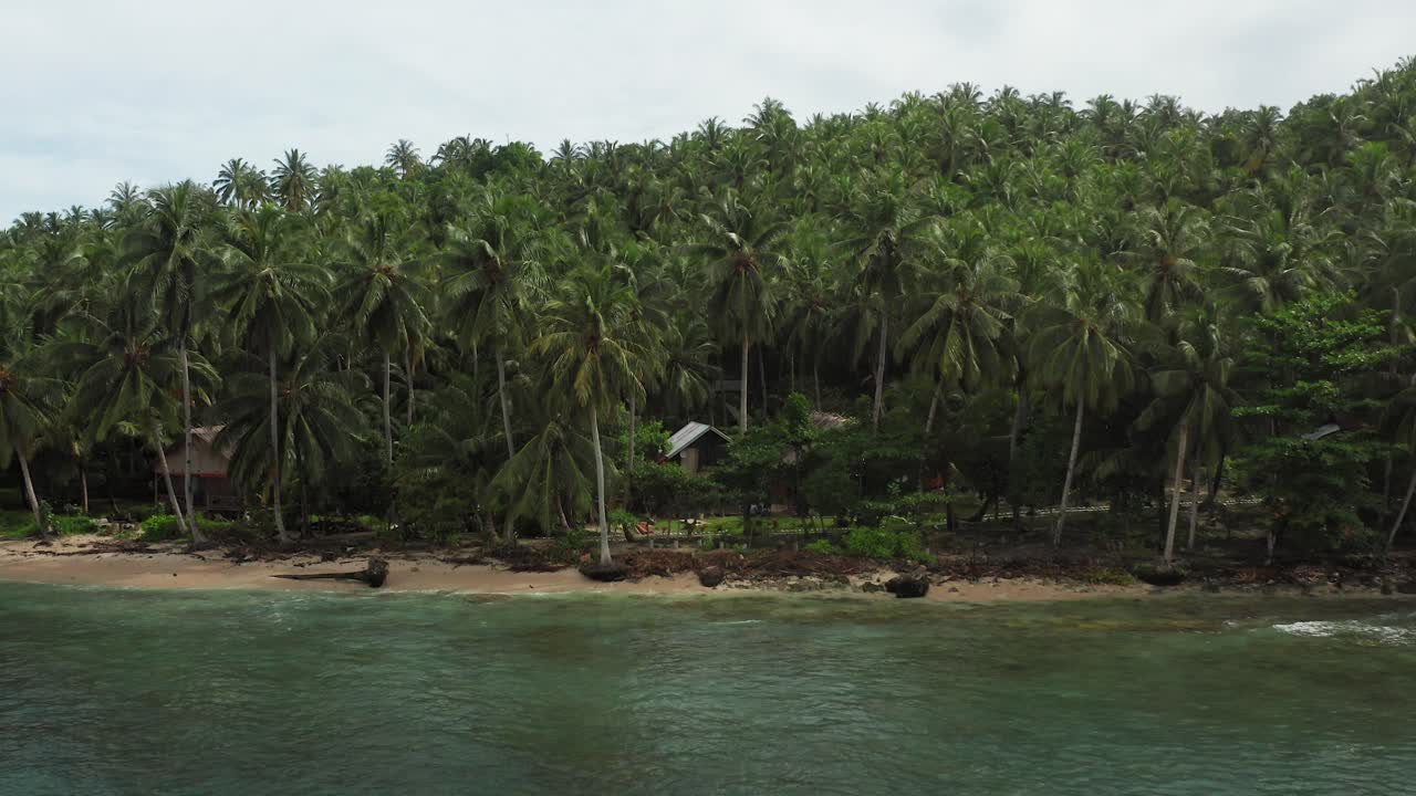 Aerial flight towards Indonesian island jungle village with empty bungalows