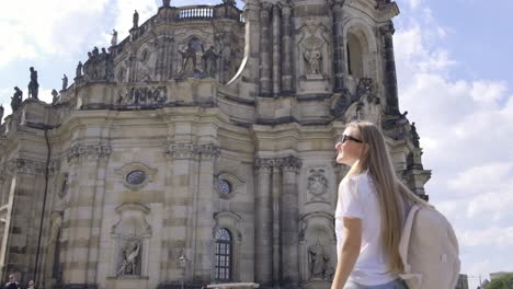a traveler with a backpack gazes at a medieval architecture masterpiece, a large building with an intricate facade, amidst a city skyline