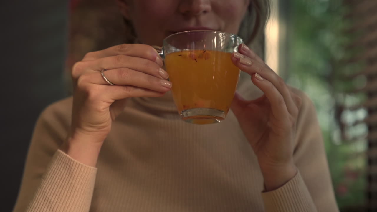 Woman drinking sea buckthorns tea from a glass cup at a restaurant
