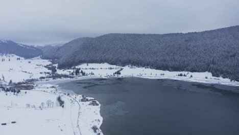 Aerial-forward-over-iced-lake-and-snowy-landscape