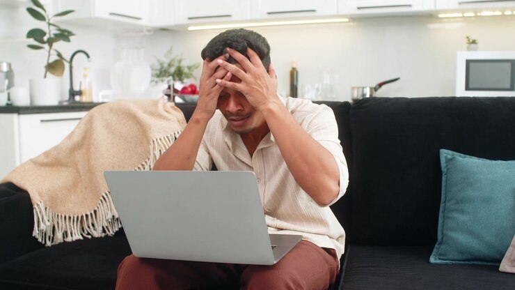 Indischer Mann liest Ablehnung auf Laptop, hält Kopf, atmet tief durch, entwickelt klaren Stufenplan zur Verbesserung seiner Arbeit