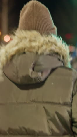 vista en primera persona de una mujer con un abrigo de invierno con una capucha de piel caminando por la noche, mientras que las personas borrosas se mueven en el fondo