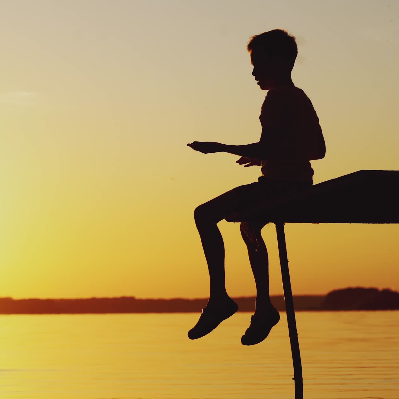 Silhouette of a boy playing on an old bridge by the river. Beautiful summer sunset
