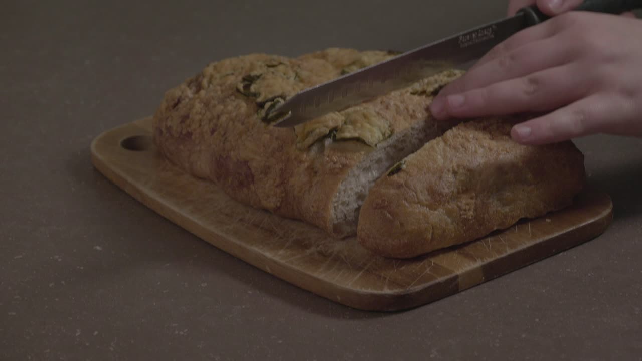 A close-up shot of some jalapeno bread being sliced on a wooden cutting board