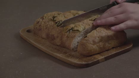 a close-up shot of some jalapeno bread being sliced on a wooden cutting board