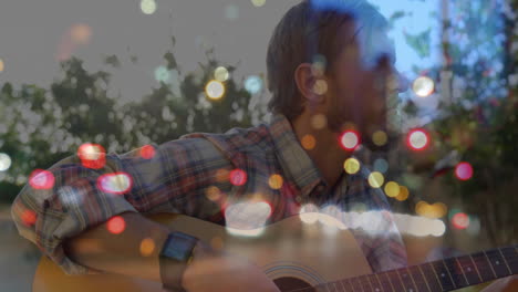 male guitarist playing acoustic guitar in garden, adding animated bokeh lights for music industry