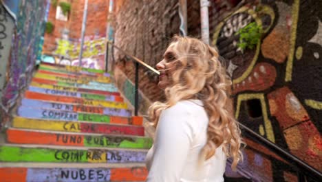 Pretty-young-blonde-girl-turning-to-the-camera-with-a-smile-in-an-alleyway-with-colorful-paintings