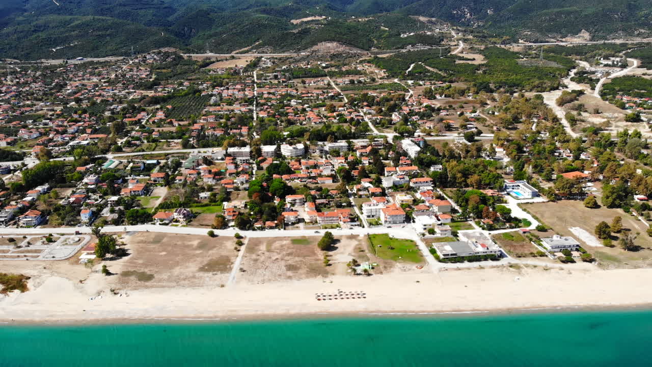 Asprovalta with multiple buildings and greenery, green hills on the background. Aegean sea coast. Long beach along the town. Sunny day. Greece