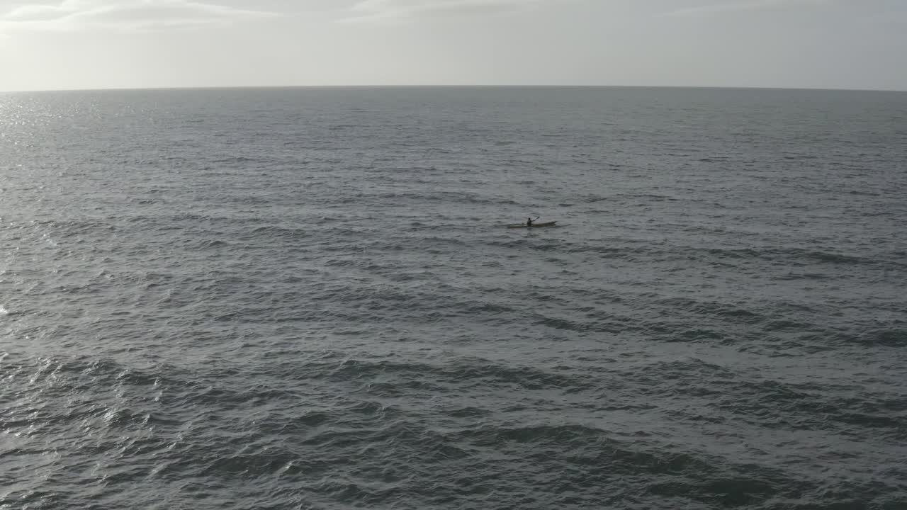 kayakista de mar solitario rema a través de la extensión vacía del océano azul acero
