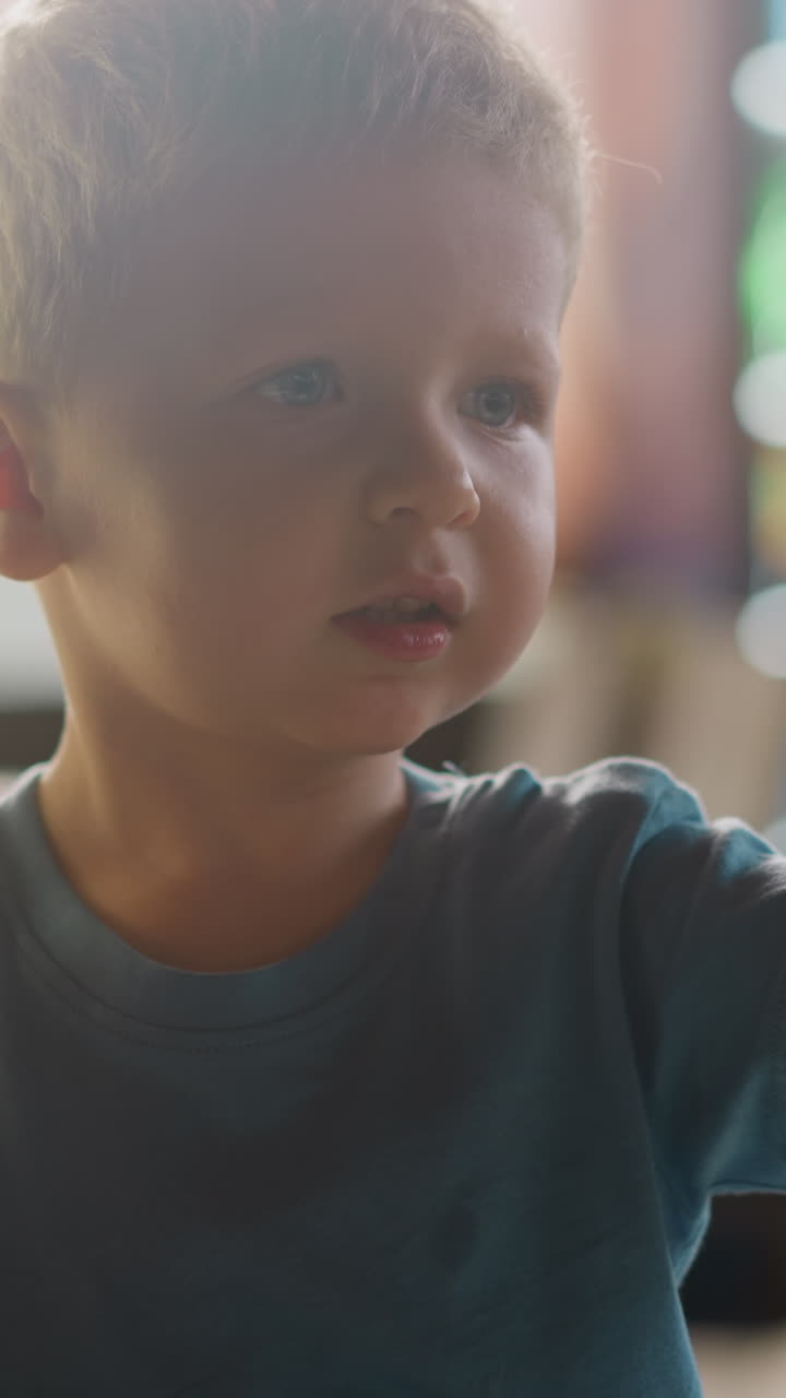 Emotional toddler boy with empty glasses put on hand talks to parent in restaurant hall lit by bright sunlight extreme close view slow motion