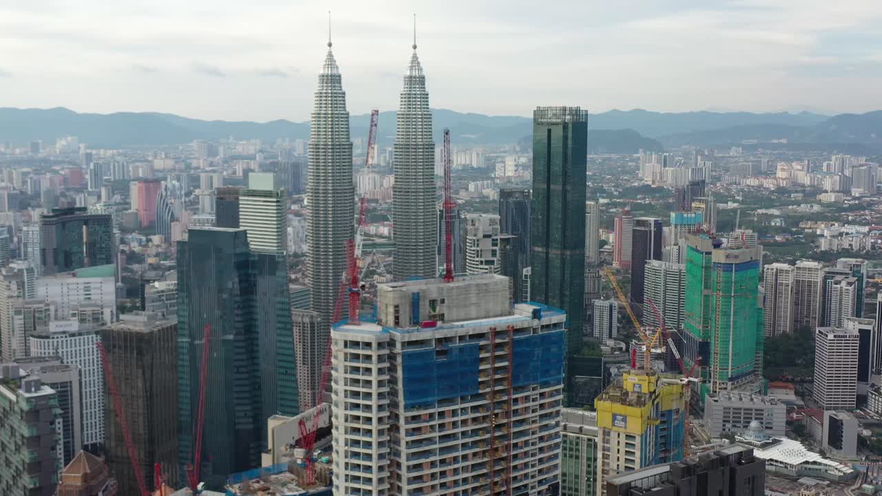 Drone fly around capturing multiple building constructions, city development with iconic petronas twin towers in the background with dense and populous cityscape, at downtown kuala lumpur, malaysia