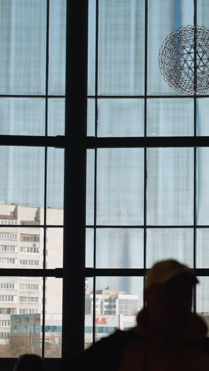 un interior de edificio moderno con grandes ventanas de piso a techo con vistas al paisaje urbano y personas moviéndose en primer plano