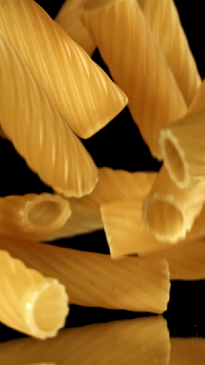 Rigatoni dorati che cadono al rallentatore su sfondo nero