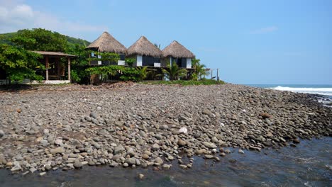 Full-is-tilting-up-shot,-scenic-view-of-beach-front-huts-on-the-bitcoin-beach-in-El-Salvador-Mexico,-on-a-bright-sunny-day