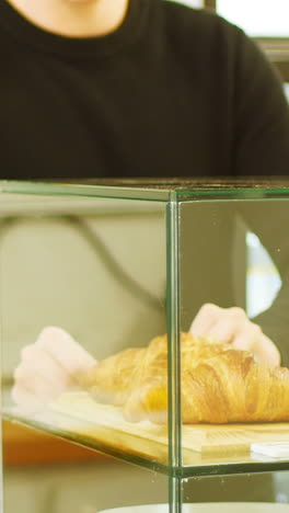 hombre manteniendo bandeja de croissants en el caso de exhibición de la cafetería