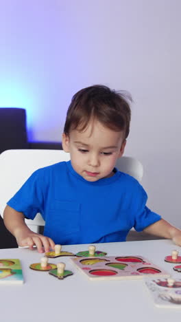 little kid in blue t-shirt runs up to a desk. lovely toddler sits down to play a game of puzzles. vertical video