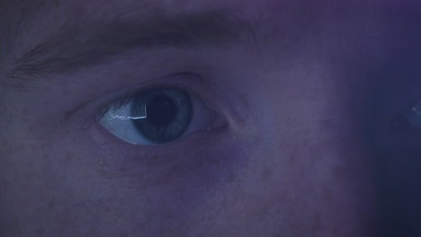 Extreme close up of a young man with blue eyes staring at a screen late at night.
