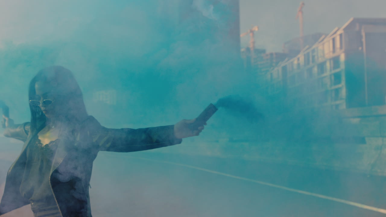 시내에서 파란색 연기 수류탄과 함께 춤을 추는 소녀 젊은 반항적인 여성은 거리에서 춤으로 창조적인 표현을 축하합니다.