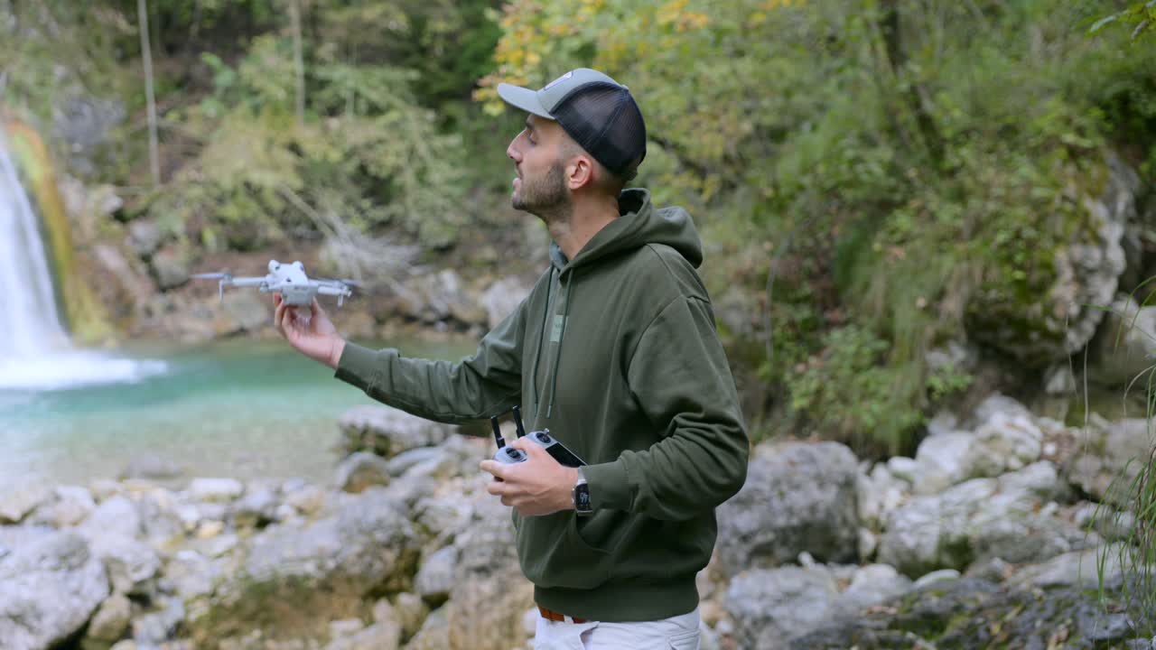 A man is launching a white drone near a waterfall in a natural setting