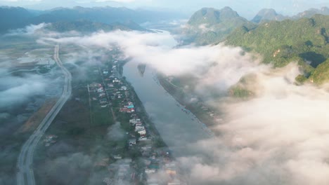drone tiro de la pequeña ciudad por el río verde debajo de la nube blanca soñadora flotando por la montaña de piedra caliza al amanecer